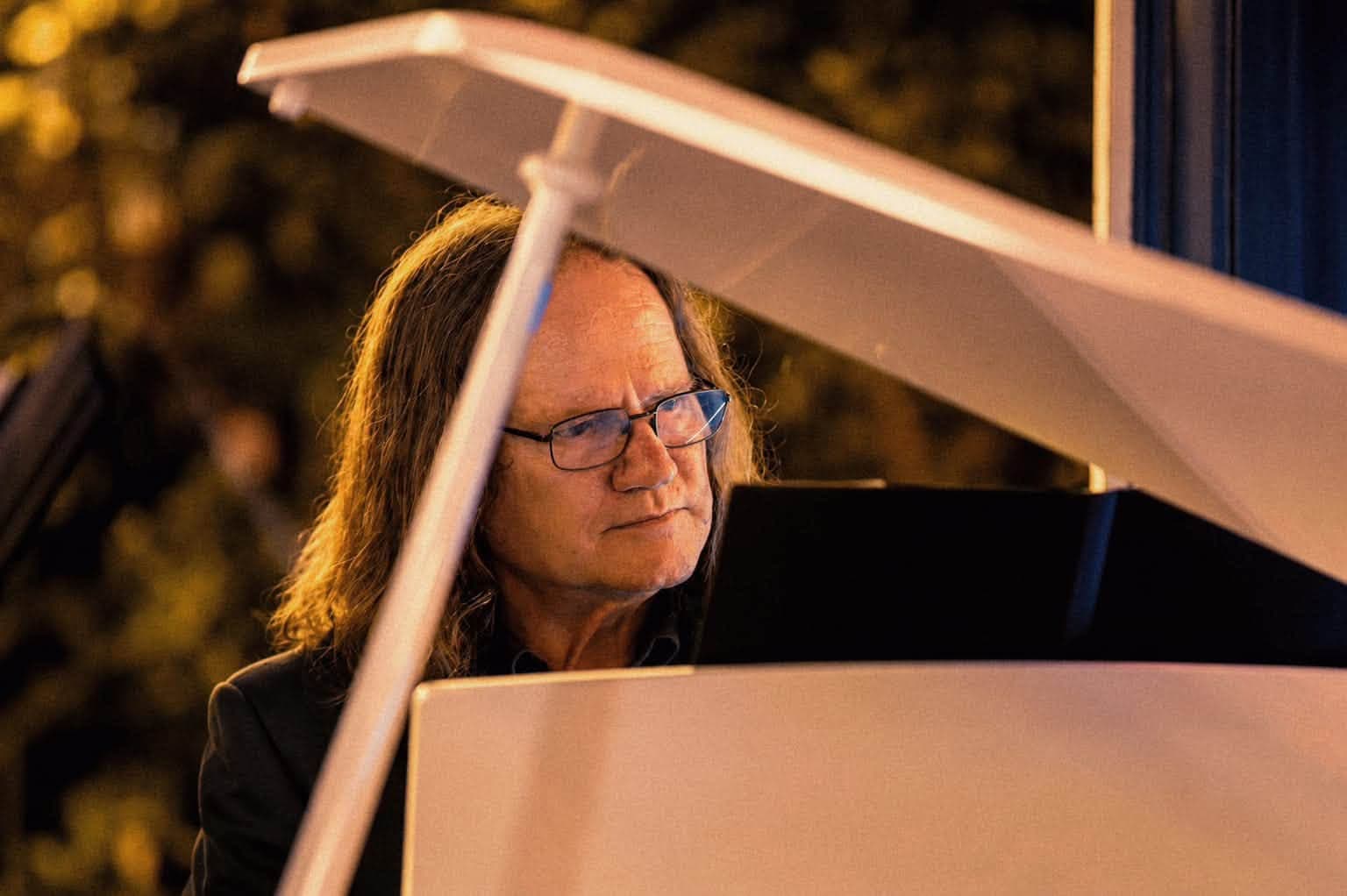 A pianist playing the white piano, seen past the raised lid